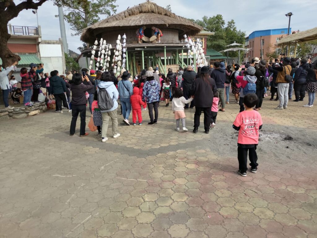 少年站在少年會所上往下丟沙子和糖果,族人圍在底下